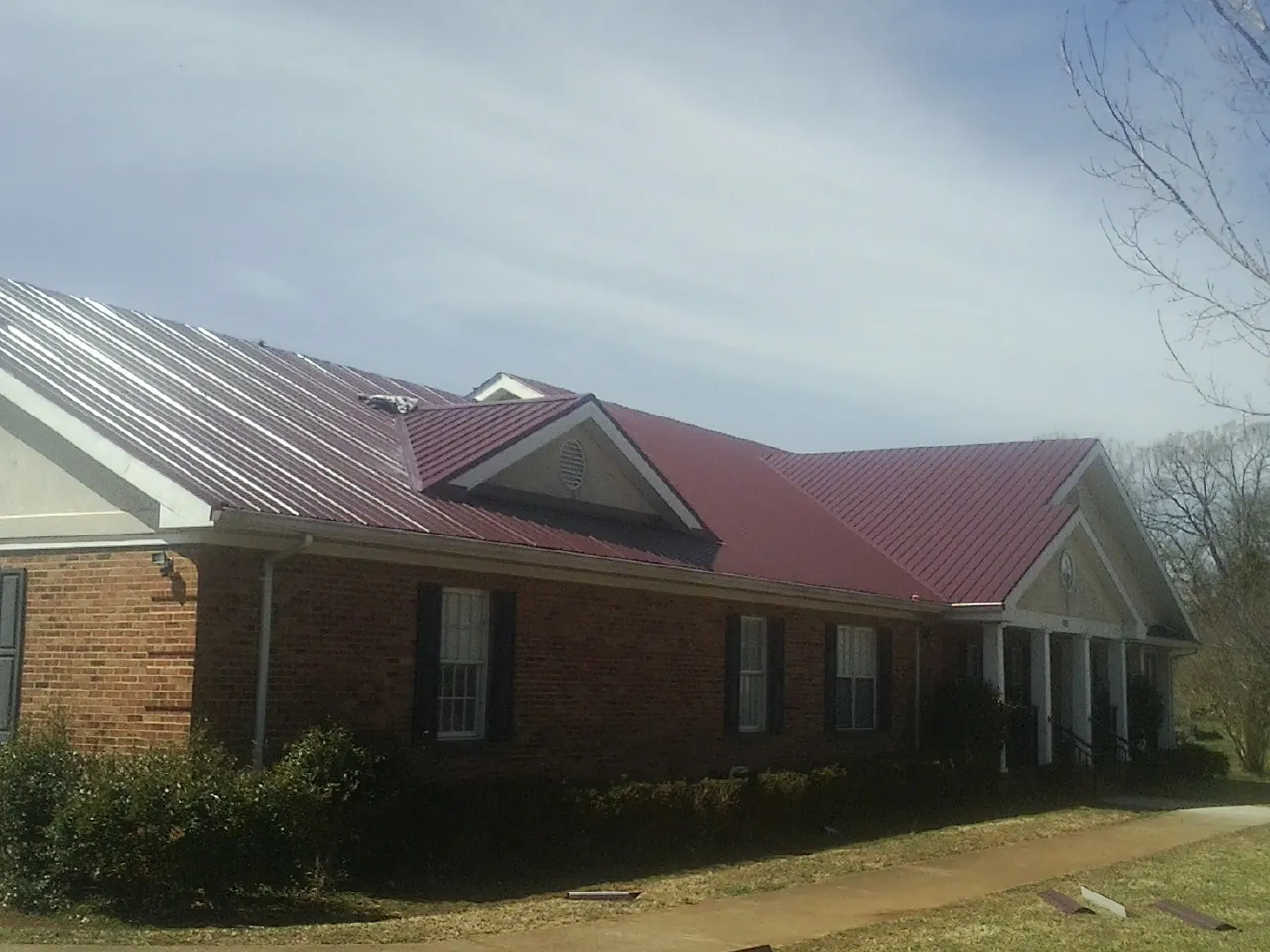 Red metal roof with gabled entries on a long brick building, from a Hail Damage Roof Repair job in Hildale