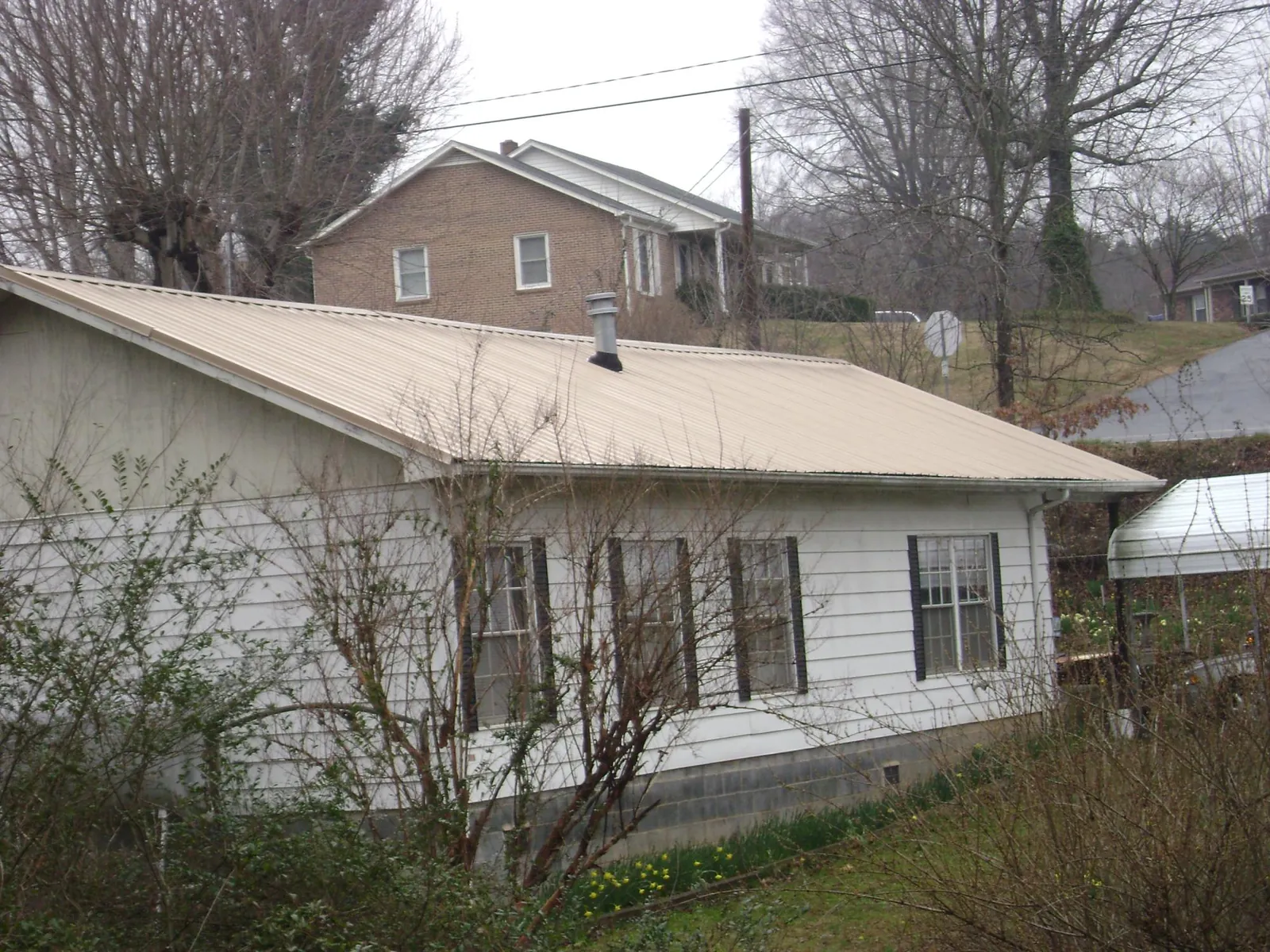 Tan metal roof on a white sided house set into a hillside — Commercial Roofing by Roofing Brothers in Hildale